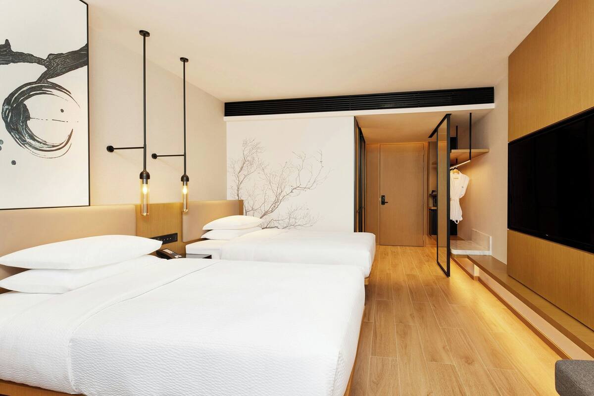 Habitación de hotel con dos camas, un espejo grande, un televisor de pantalla plana y una obra de arte colgada en la pared.