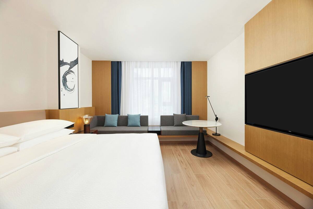 Una habitación de hotel moderna con una cama grande, un sofá, una mesita y un televisor.