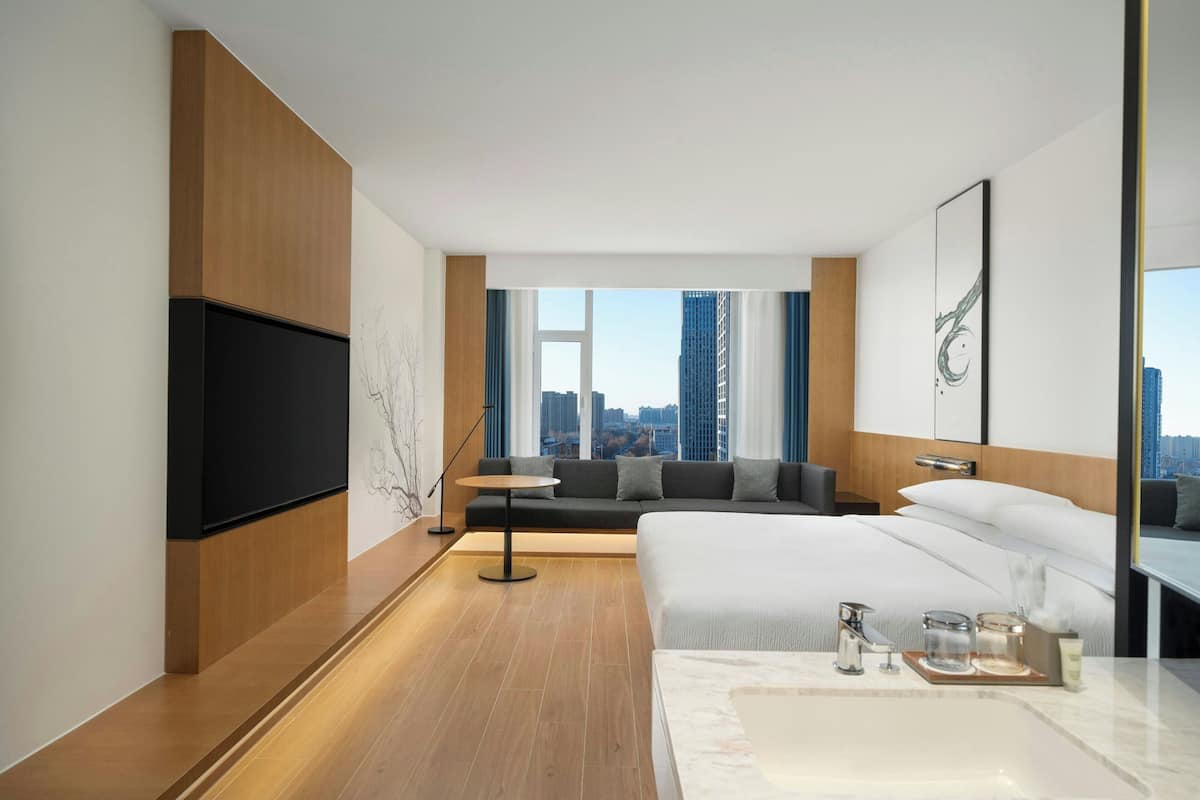 Habitación de hotel moderna con una cama grande, televisión, sofá y vista a la ciudad.