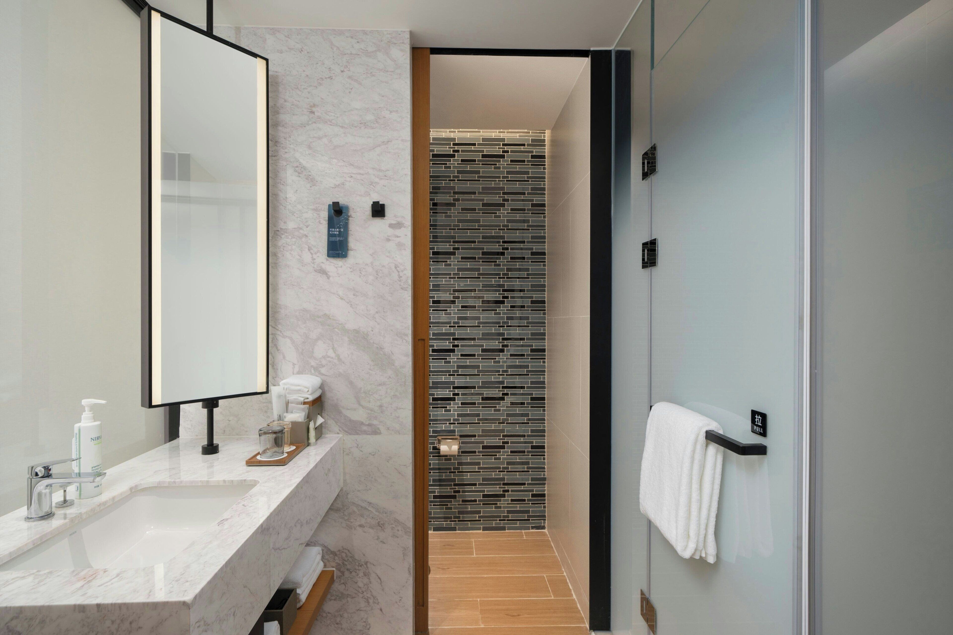 A modern bathroom with a marble sink, a large mirror, a glass shower enclosure, and a towel rack.