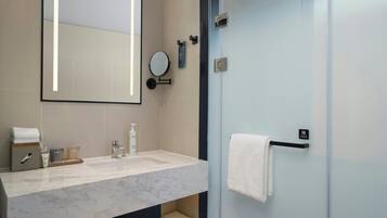 A modern bathroom with a marble sink, a large mirror, a glass shower enclosure, and a towel rack.