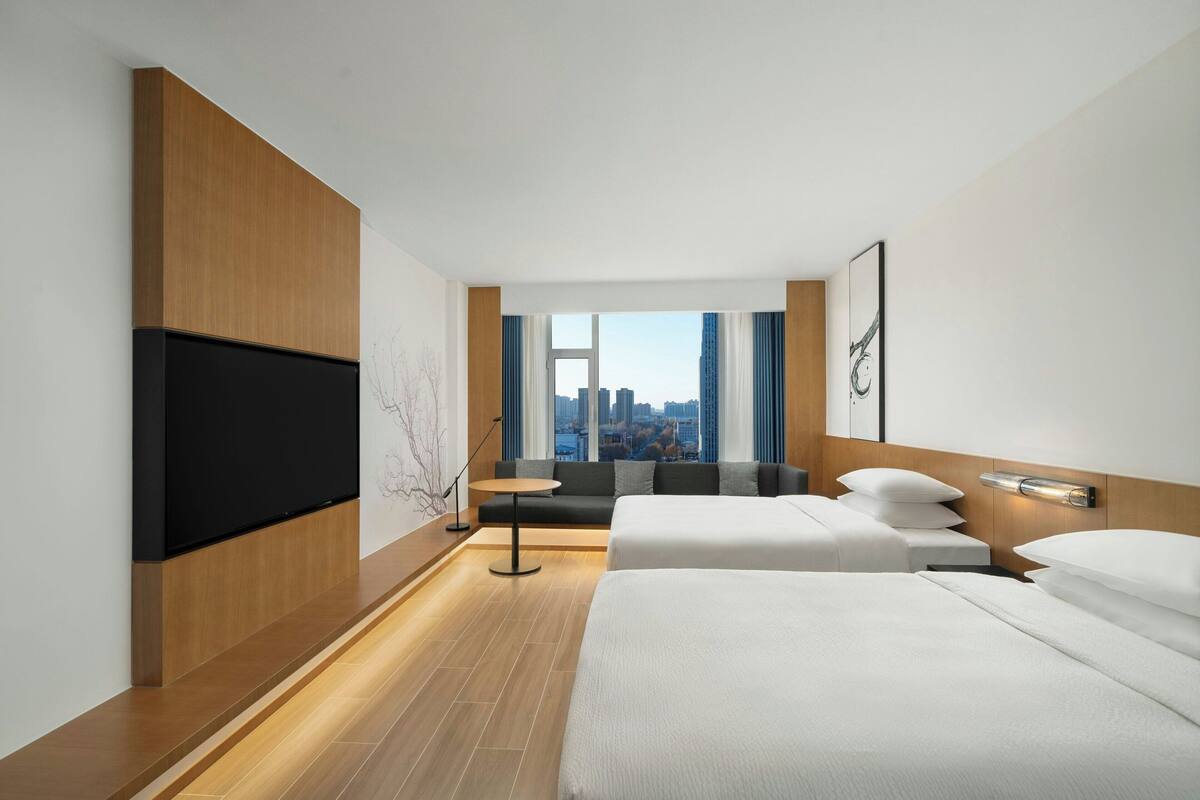Una habitación de hotel moderna con una cama grande, un televisor de pantalla plana, un sofá y vistas a la ciudad.