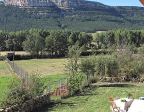 A grassy outdoor area with a stone wall, a metal gate, and a table with chairs set up for dining. - Rustic Country House near Laguna Negra with Mountain Views and Garden (CIDONES)