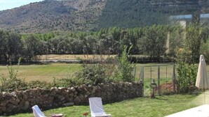 Un espacio al aire libre con césped, un muro de piedra, una silla lounge blanca y una mesa.