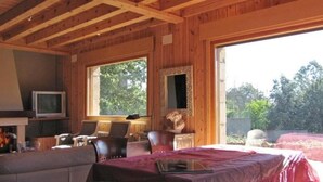 Una cabaña de madera con cama, televisión y ventana con vistas a la vegetación.
