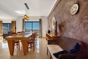 A dining area with a wooden table and chairs, a wicker sofa, and a view of the outdoors.