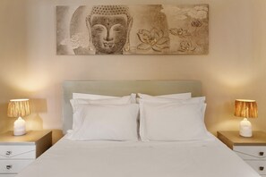 A bed with white bedding, two bedside tables with lamps, and a wall-mounted artwork.