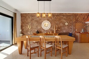A dining area with a wooden table and chairs, a hanging light fixture, and a brick wall with decorative items.