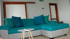 A modern living room with a teal sofa, a small round table, and a wooden-framed door.