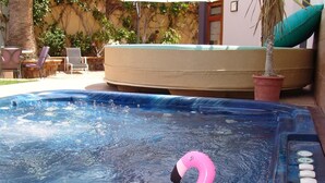 A hot tub with a pink flamingo float, surrounded by outdoor furniture and a potted plant.