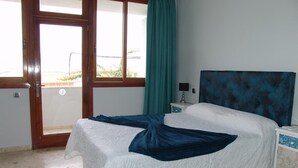 A bedroom with a bed, a nightstand, a window with curtains, and a door.