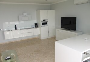 Une cuisine moderne avec des meubles blancs, un four encastré, un four à micro-ondes et un grand téléviseur à écran plat.