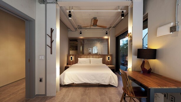 Un dormitorio moderno con una cama grande, cabecera de madera, mesitas de noche, un escritorio con silla y un ventilador de techo.