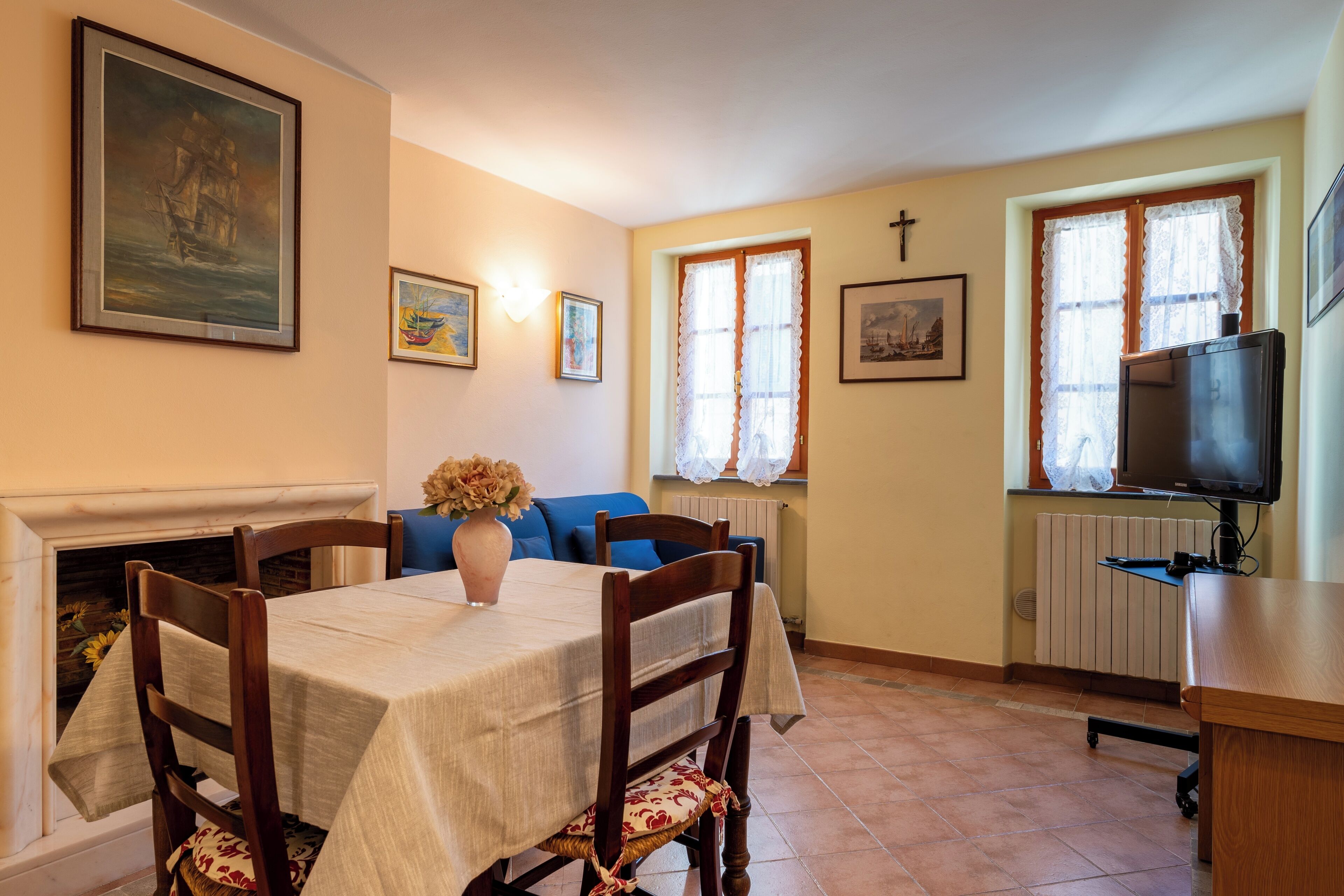 Un coin repas comprenant une table, des chaises, un vase avec des fleurs, une cheminée et un téléviseur posé sur un meuble.