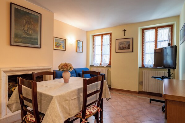A dining area with a table, chairs, a vase with flowers, a fireplace, and a television on a stand. - Suite Carla cozy apartment in Petrasanta center (Pietrasanta)