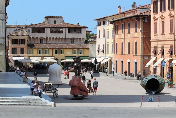 A public square with historical buildings, a statue, and a large sculpture.
