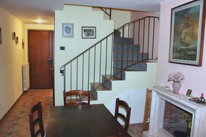 A dining area with a wooden table and chairs, a staircase with a metal railing, and a fireplace with a vase of flowers.