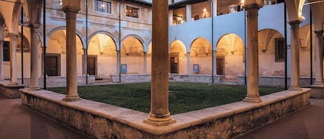 Un cortile con archi e colonne, una zona verdeggiante e un edificio con numerose finestre.