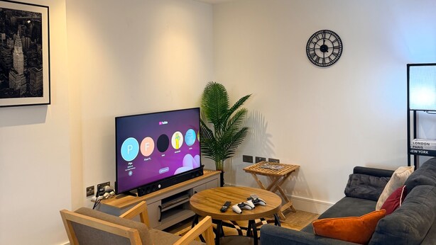 Ein modernes Wohnzimmer mit Fernseher, einer Uhr, einer Pflanze, einem Sofa und einem Couchtisch.