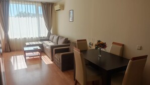 A living room with a sofa, a coffee table, a dining table with chairs, and a window with curtains.