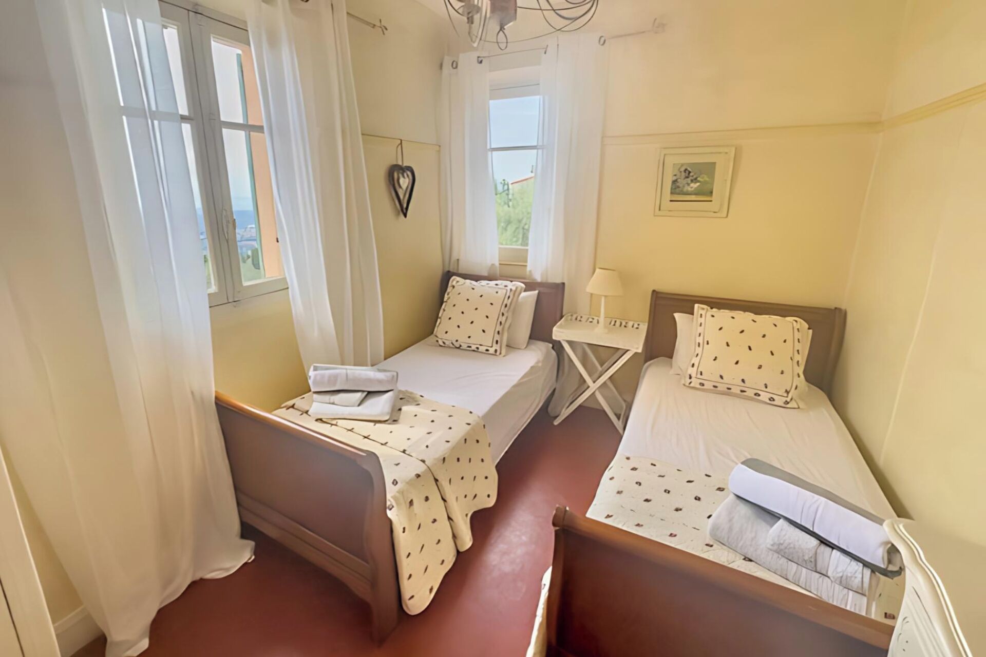 Una habitación con dos camas individuales, una mesita y un ventanal con cortinas.