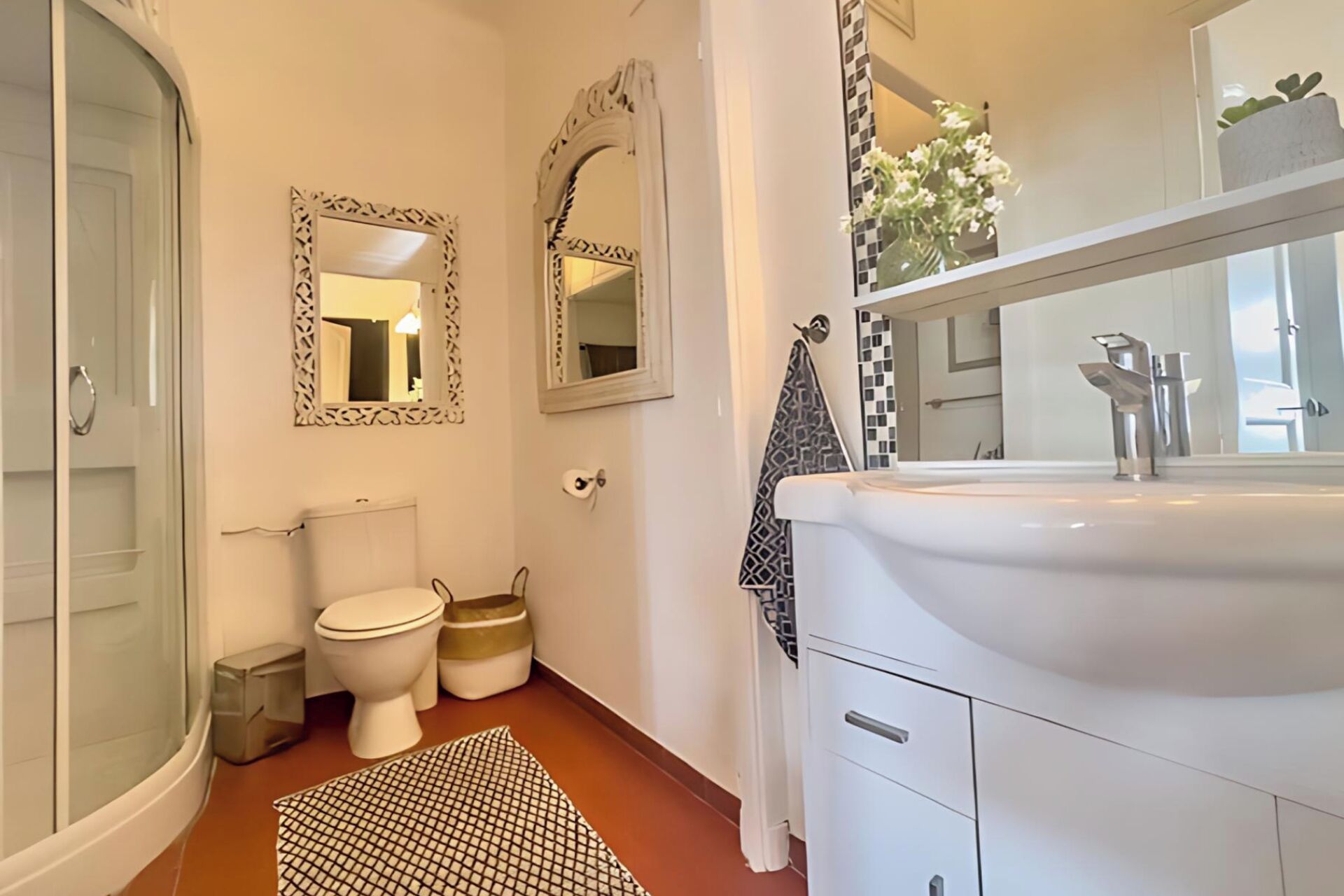 A modern bathroom with a glass shower enclosure, a white sink with a mirror above it, and two toilets.