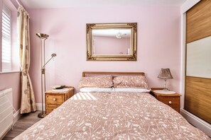 Een slaapkamer met een groot bed, twee nachtkastjes, een vloerlamp, een spiegel en een raam met gordijnen.