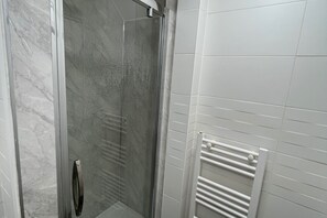 Een badkamer met een douchecabine van glas, witte betegelde wanden en een witte handdoekhouder.