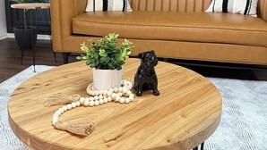 Een ronde houten tafel met een bloempot, een kralenketting en een beeldje van een zwarte hond.