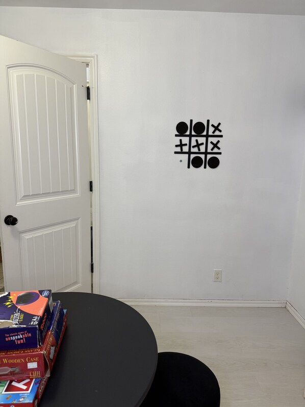 Um quarto com uma porta branca, uma mesa preta e uma parede com o desenho de um jogo da velha.