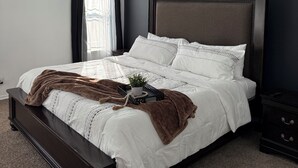 Een net opgemaakt bed met een bruine plaid, een nachtkastje met een afstandsbediening en een plafondlamp.