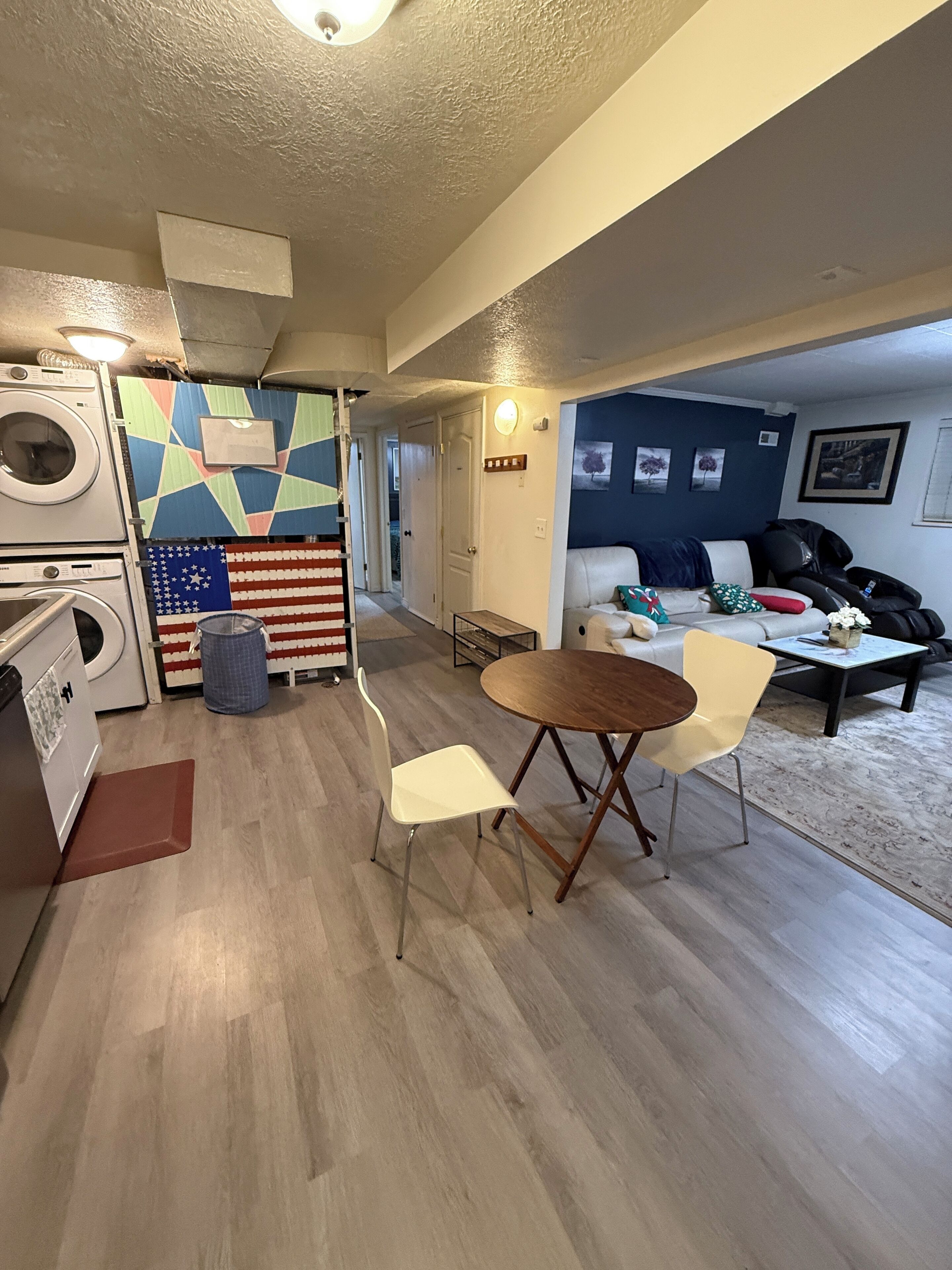 Un espai vital compacte amb una zona de cuina que inclou una rentadora, una taula de dinar amb dues cadires i un sofà.