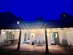 Ein möblierter Patio mit Tisch und Stühlen, ein überdachter Sitzbereich und eine Tür zum Innenbereich.