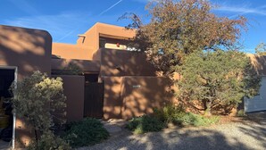 A residential building with a gravel driveway, a wooden gate, and a tree in the foreground.