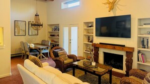 A living room with a fireplace, a mounted deer head, a television, and a dining area with chairs and a table.