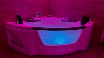 Un moderno jacuzzi iluminado en rosa, con interfaz digital, butaca de masaje incorporada y panel de control.