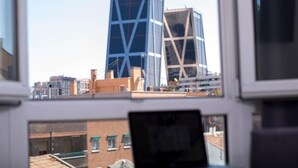 A view of a building with the name 'Bankia' on it, seen through a window with a laptop on a desk. - HOTEL CABALLERO ERRANTE (Madrid)