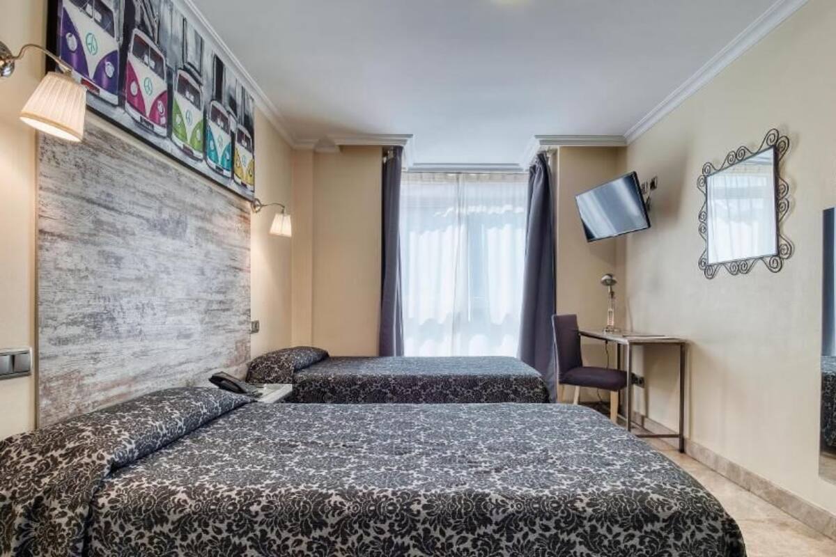 A hotel room with two beds, a TV, a desk, and a large window with curtains.