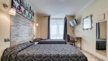 Ein Hotelzimmer mit zwei Betten, einem Fernseher, einem Schreibtisch und einem großen Fenster mit Vorhängen.