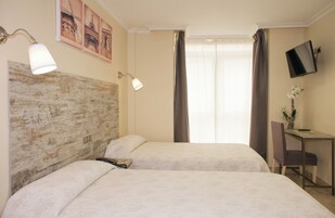 A hotel room with two beds, a desk, a chair, a TV, and a window with curtains.