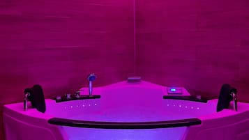 A modern spa room with a large bathtub, pink ambient lighting, and a wooden wall.