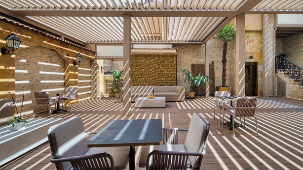 An outdoor patio area with a striped floor pattern, a central seating area with a sofa and chairs, and a brick wall in the background. - HOTEL CABALLERO ERRANTE (Madrid)