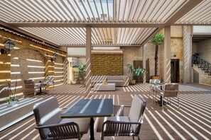 An outdoor patio area with a striped floor pattern, a central seating area with a sofa and chairs, and a brick wall in the background. - HOTEL CABALLERO ERRANTE (Madrid)