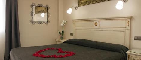 A hotel room with a bed, a nightstand, a mirror, and a wall-mounted light fixture.