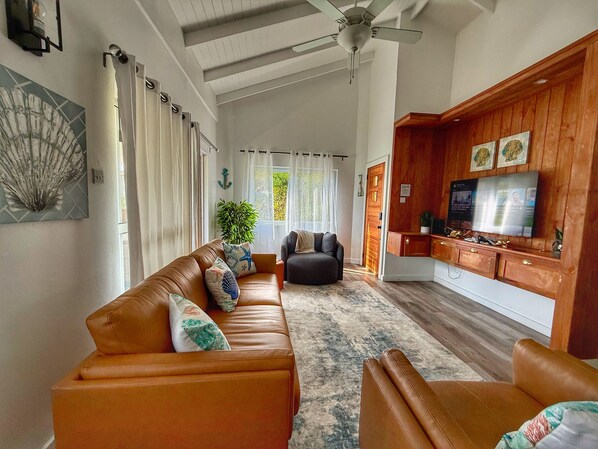 A spacious living room with a brown leather sofa, a black armchair, and a wooden cabinet with a TV.