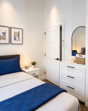 A bedroom with a bed, bedside table, nightstand, dresser, and a mirror.