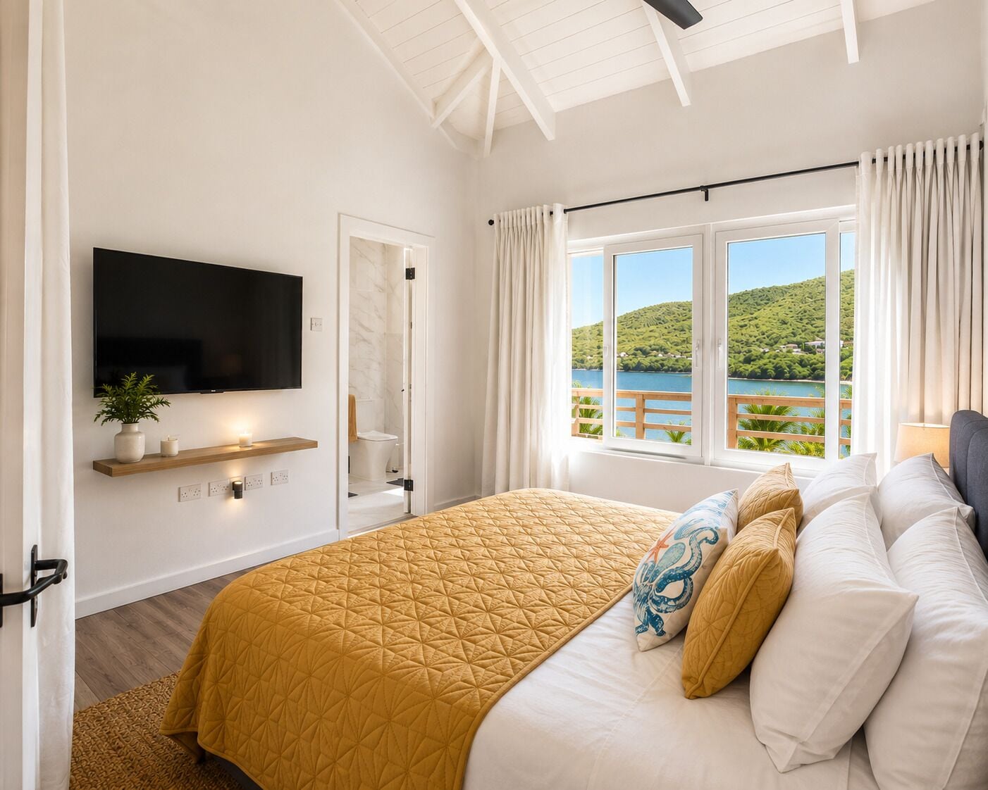 A bedroom with a bed, a TV, a window with a view of a lake and hills, and a door leading to a bathroom.