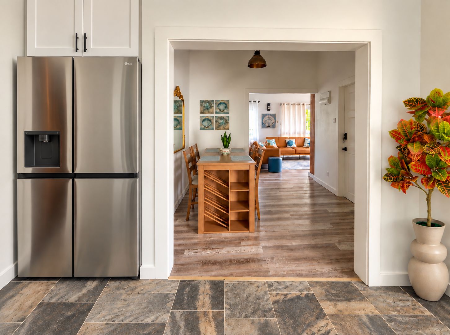 Een moderne keuken met een roestvrijstalen koelkast, een eethoek met een houten tafel en stoelen, en een woonkamer met een bank en decoratieve wandkunst.