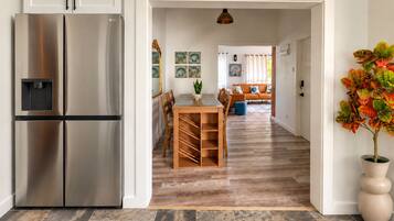 Eine moderne Küche mit einem Edelstahlkühlschrank, ein Essbereich mit Holztisch und Stühlen sowie ein Wohnzimmer mit Sofa und Wanddekoration.