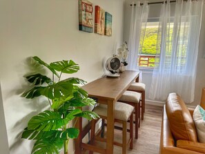 A dining area with a wooden table, chairs, a potted plant, a fan, and a sofa.